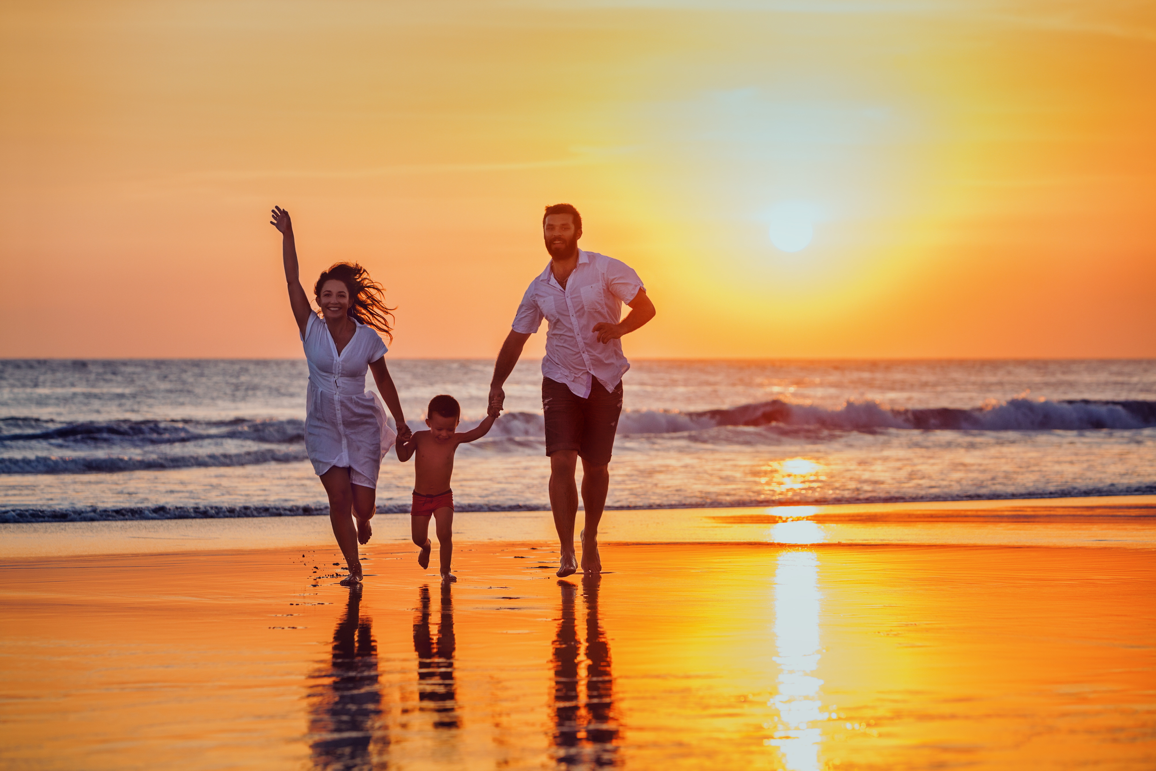 Father, mother, baby have a fun on sunset beach - Pharmacists Mutual